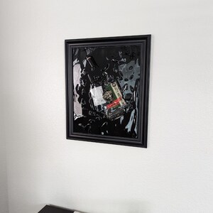 May include: A black framed picture with a clear resin background. A glass bottle and a small red, white, and green label are embedded in the resin. The label reads "SAFETY INSTRUCTIONS".
