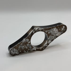 May include: A black bookend with silver flecks embedded in the resin. The bookend is shaped like a flattened teardrop with a rounded hole in the center.
