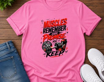 May include: A bright pink short-sleeved t-shirt featuring a graphic print with the text MUSCLES REMEMBER EVERY PROMISE YOU KEEP in black and red lettering, accompanied by an illustration of a black dumbbell and a black protein shaker bottle.