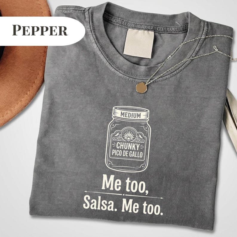 May include: A gray t-shirt with a white graphic of a jar labeled "Chunky Pico De Gallo" and the text "Me too, Salsa. Me too." A silver necklace with a small pendant is on the shirt.