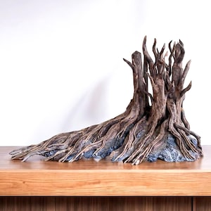 Può includere: Scultura dettagliata in legno di deriva marrone con intricati dettagli di radici e rami. La scultura è montata su una base grigio scuro, creando un'estetica naturalistica. Il pezzo è esposto su una superficie di legno su sfondo bianco.