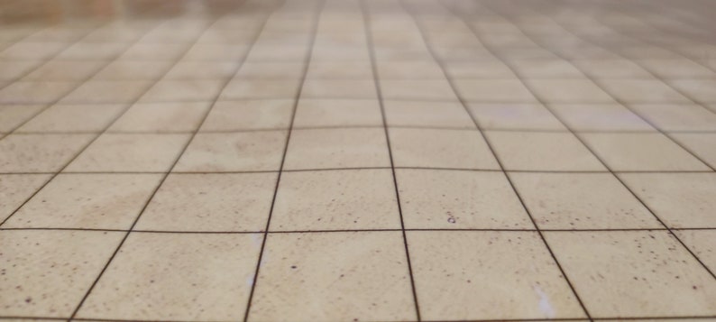 Puede incluir: Superficie beige con patr&oacute;n de cuadr&iacute;cula, posiblemente una mesa o suelo, con l&iacute;neas oscuras que crean un efecto de baldosas. La superficie tiene un aspecto ligeramente texturizado, con sutiles variaciones de color.