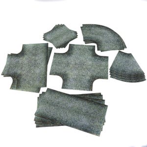 Könnte beinhalten: Eine Sammlung verschieden geformter, strukturierter, grauer Stoffstücke. Die Stücke umfassen Quadrate, gebogene Abschnitte und kreuzförmige Designs. Der Stoff hat ein gesprenkeltes Aussehen, und die Stücke sind auf weißem Hintergrund angeordnet.
