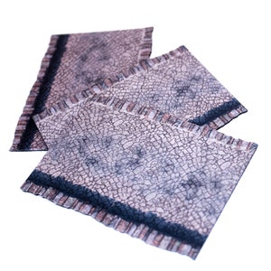 Puede incluir: Tres posavasos rectangulares con un patrón texturizado tipo mosaico en tonos grises y marrones. Cada posavasos tiene un borde azul oscuro y un borde decorativo. Los posavasos están dispuestos en ángulo sobre un fondo blanco.