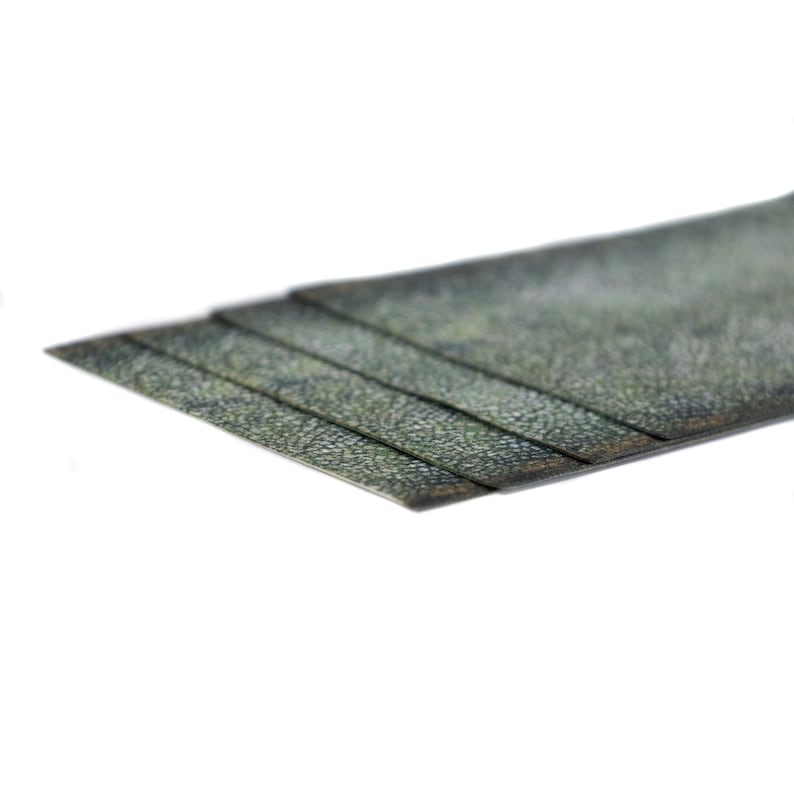 May include: A close-up shot of a stack of textured, dark green material. The material is layered, with each layer slightly offset, creating a stepped effect. The surface has a speckled pattern, and the edges are clean and straight.