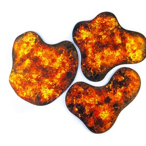 May include: Three abstract, irregularly shaped coasters with a fiery, textured design. The coasters feature a blend of orange, yellow, and brown hues, creating a lava-like appearance. The edges are dark brown, and the background is white.
