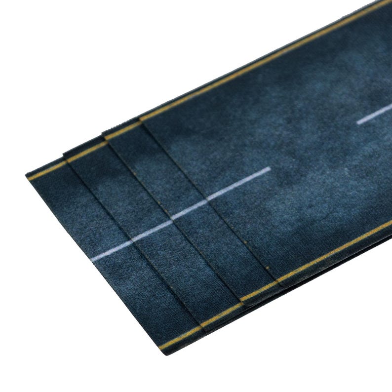 May include: A section of a miniature road, featuring a dark blue-gray asphalt surface with a white lane divider and yellow edge lines. The road is layered, suggesting a modular design for model building or crafting projects.