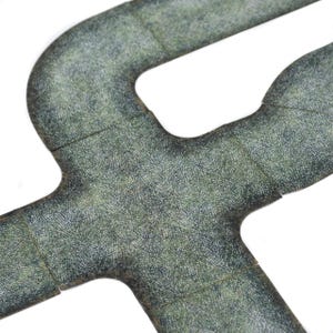 May include: Overhead shot of interlocking, textured, grey-green game tiles. The tiles feature a road-like design with curved and straight sections. The surface has a detailed, speckled pattern.