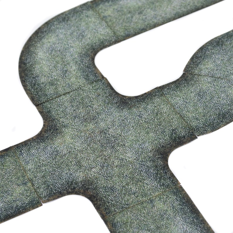 May include: Overhead shot of interlocking, textured, grey-green game tiles. The tiles feature a road-like design with curved and straight sections. The surface has a detailed, speckled pattern.