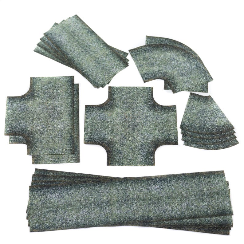 May include: A selection of grey, textured terrain tiles in various shapes, including straight sections, curves, and intersection pieces. The tiles are designed for tabletop gaming and miniature wargaming, providing a modular landscape.