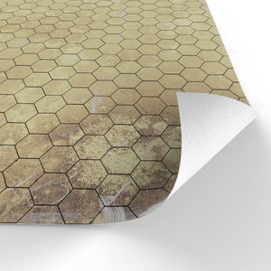 Puede incluir: Primer plano de una secci&oacute;n de un patr&oacute;n de baldosas hexagonales en tonos beige y marr&oacute;n. Las baldosas tienen contornos oscuros y la superficie tiene un aspecto envejecido y desgastado. Una esquina del material est&aacute; doblada, revelando un reverso blanco.