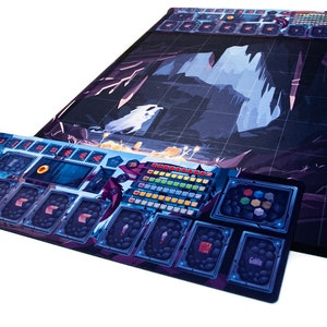 May include: Two-piece board game set with a fantasy theme. The main board features a cave scene with a grid overlay. The smaller board has spaces for cards and tokens. The color palette includes blues, purples, and whites.