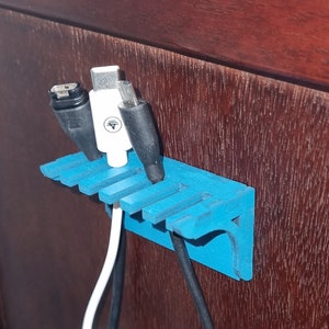 以下が含まれることがあります： 6つのスロットが付いた青いプラスチック製のケーブルオーガナイザー。3本のケーブルがオーガナイザーに接続されており、2本は黒、1本は白です。