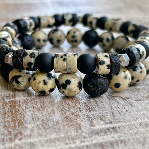 May include: Two bracelets made of black, white, and gray beads. The bracelets are made of dalmatian jasper, lava rock, and black onyx beads.