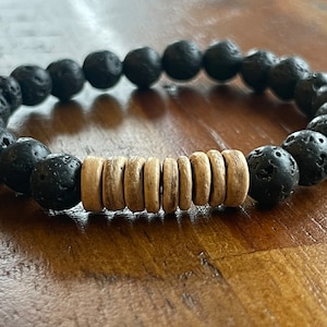 May include: A black lava rock and wood bead bracelet. The bracelet has a row of wood beads in the center and is made with black lava rock beads.