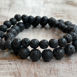 May include: A black lava rock beaded bracelet. The bracelet is made of round, black beads with a rough, textured surface.