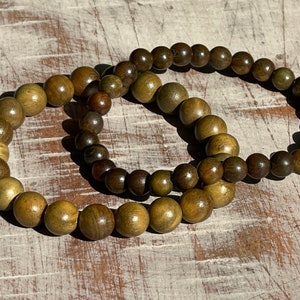 May include: Two wooden bracelets with brown and green beads. The bracelets are made of natural wood and have a rustic look.