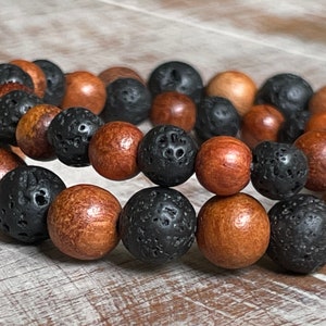 May include: Two bracelets made of black lava rock and brown wooden beads. The bracelets are stacked on top of each other.