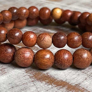 May include: Two brown wooden beaded bracelets stacked on top of each other. The beads are round and have a smooth, polished finish.