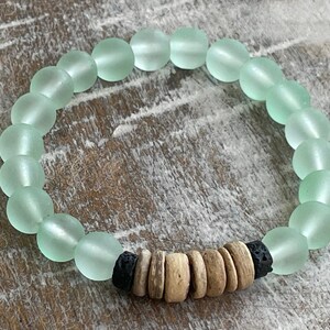 May include: A light green glass bead bracelet with brown wood and black lava rock beads.
