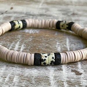 May include: A pink and black beaded bracelet with white and black patterned beads. The bracelet is made of round beads and is strung on a stretchy cord.