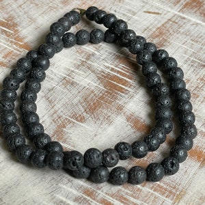 May include: A black lava rock beaded necklace. The beads are round and have a rough, textured surface.