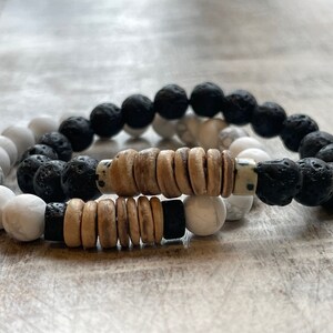 May include: Two bracelets made with black lava rock beads, white howlite beads, and brown wood beads.
