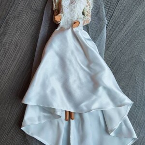 May include: A white bridal gown with a lace bodice and a tulle veil. The doll is wearing a white headband with a flower.