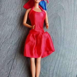 May include: A vintage Barbie doll wearing a red satin dress with a blue bow. The doll has blonde hair and blue eyes.