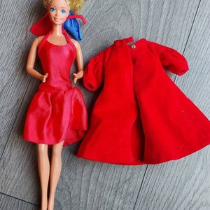 May include: A vintage Barbie doll wearing a red dress and a blue ribbon. The doll is also wearing a red velvet coat.