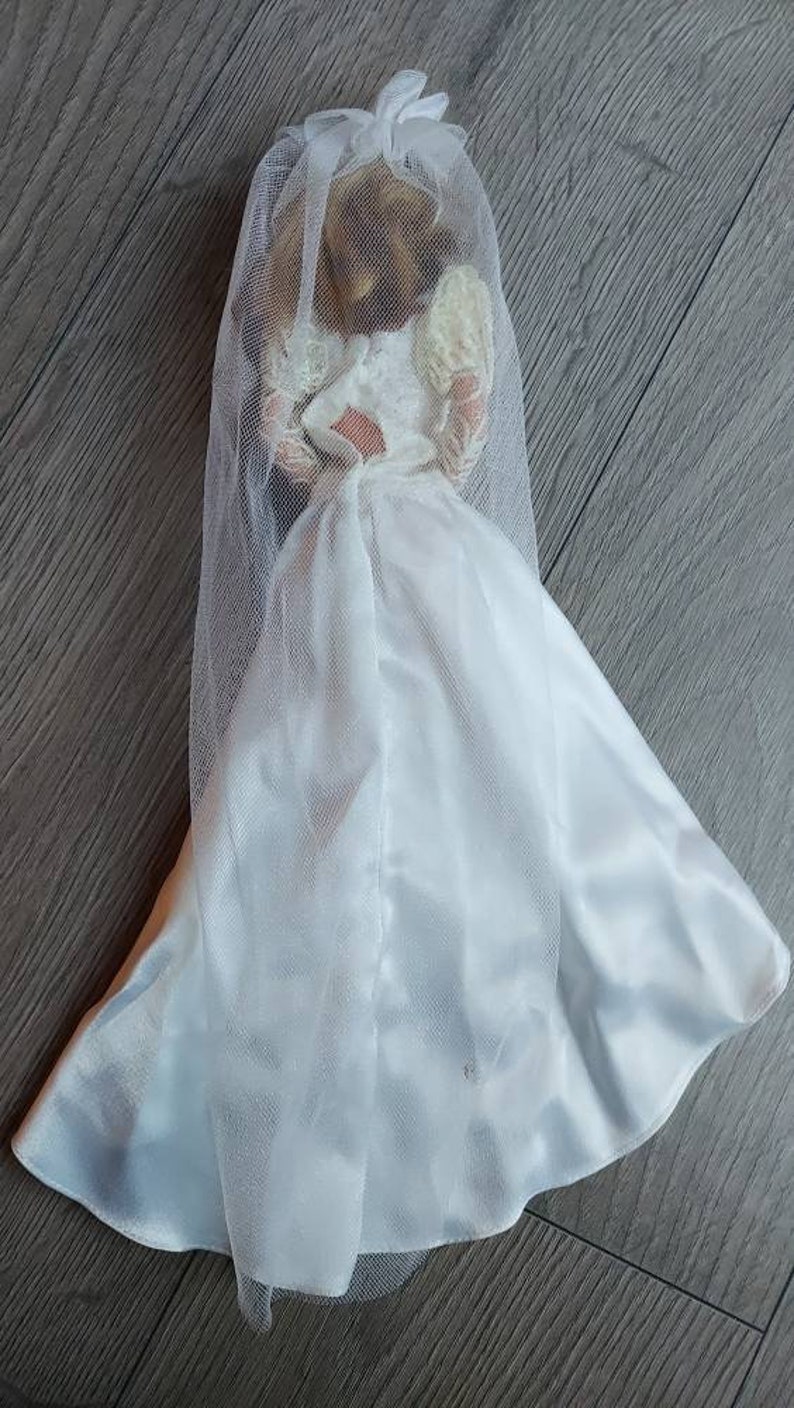 May include: A white bridal gown with a long veil. The gown is made of a satin-like fabric and has a fitted bodice and a flowing skirt.