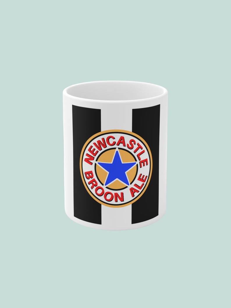 May include: White ceramic mug with black vertical stripes and a circular emblem. The emblem features a blue star in a gold circle, with the words "NEWCASTLE BROON ALE" in red lettering. The mug is cylindrical.