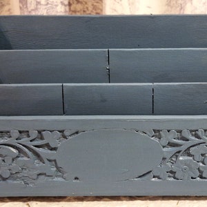 Puede incluir: Un organizador de escritorio de madera azul con tres compartimentos y un diseño tallado ornamentado. El organizador tiene un óvalo tallado en el centro y patrones florales en los lados.