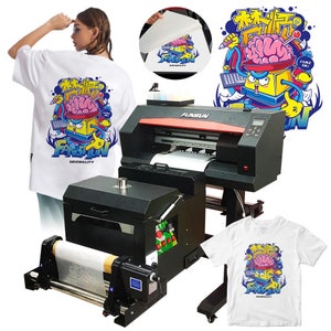 May include: A black and red digital printing machine with a white t-shirt being printed with a colorful graphic design featuring a cartoon brain in a box. The design includes the text "FANSUN ORIGINALITY" and "COME ON!" in English and Chinese characters. The machine has a roll of white transfer paper and a white t-shirt on a stand.