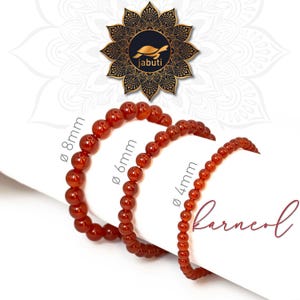 Könnte beinhalten: Drei Perlenarmbänder aus glatten, runden, dunkelorangen Karneolsteinen. Die Armbänder sind nach Größe sortiert und mit Text beschriftet, der die Perlendurchmesser von 8mm, 6mm und 4mm angibt. Ein Logo mit einer Schildkröte und dem Text jabuti ist sichtbar.