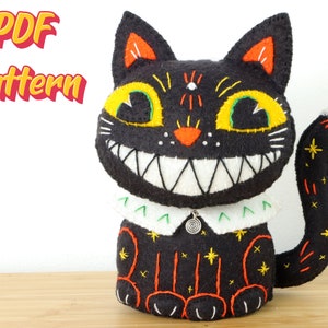 May include: A black cat plush toy with a large, grinning mouth and yellow eyes. The cat features orange and yellow detailing, a white collar, and a curled tail. The words "PDF Pattern" are visible in the image.