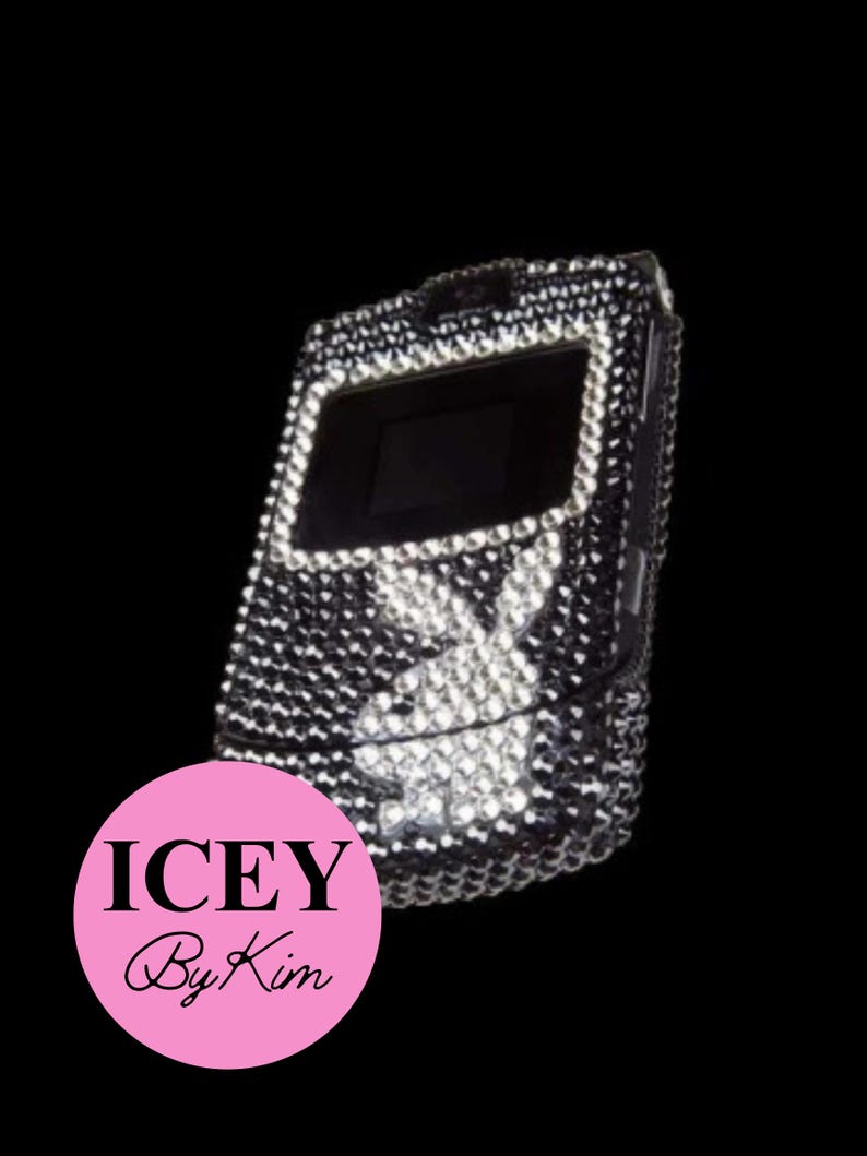 Pu&ograve; includere: Un telefono a conchiglia tempestato di cristalli neri e argentati. Il telefono presenta uno schermo nero e un logo a forma di coniglio bianco. Il telefono &egrave; decorato con molti piccoli cristalli. Il testo "ICEY By Kim" &egrave; in un cerchio rosa.