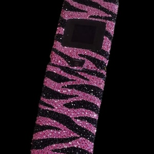 May include: A bedazzled flip phone case with a zebra stripe pattern. The case features alternating stripes of black and pink glitter, creating a sparkling, eye-catching design. The phone case is set against a black background.