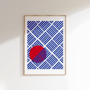 Könnte beinhalten: Gerahmter Kunstdruck mit geometrischem Design. Das Kunstwerk zeigt ein Muster aus blauen diagonalen Linien, die einen Web-Effekt bilden, mit einem roten Kreis in der Mitte. Der Druck ist in einem hellbraunen Holzrahmen.