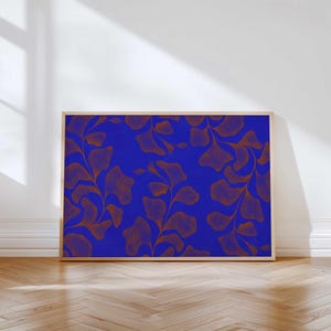 May include: A framed art print featuring a vibrant blue background with a repeating pattern of stylized, rust-colored leaves and stems. The artwork is displayed in a light-colored wooden frame, adding a touch of warmth to the design.