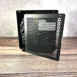 May include: A black metal computer case with a honeycomb mesh front panel. The case is open, revealing internal components and wiring. The case sits on a wooden surface.