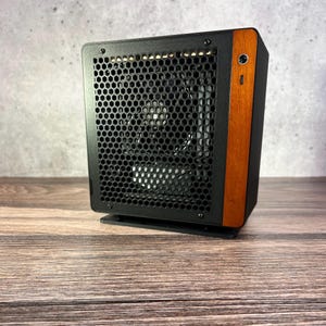 May include: A compact computer case featuring a black metal frame with a hexagonal honeycomb mesh front panel and a vertical wood grain accent strip on the right side, including a circular power button and a small vertical indicator light.