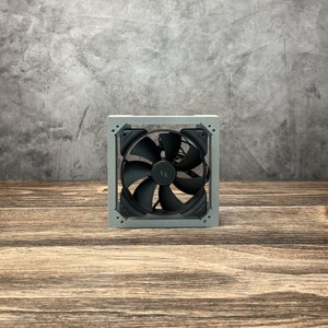 Puede incluir: Un ventilador de ordenador plateado con una hélice de ventilador negra dentro de un marco plateado.