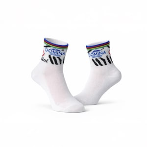 May include: Two white athletic socks with a multi-coloured striped band at the top. The socks display the word "DOMINA" in blue and black zebra stripes. The brand name "lini" is printed on the side.