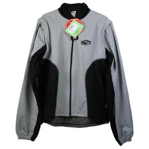 Pode incluir: Uma jaqueta de ciclismo cinza e preta com zíper completo e um logotipo no peito esquerdo. A jaqueta tem um forro de malha e uma faixa reflexiva nas costas.