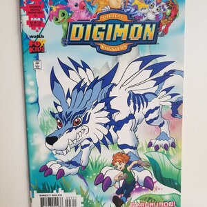 May include: A comic book cover featuring a blue and white wolf-like creature with purple claws and a red-haired boy in a green shirt. The title of the comic is "Digimon Digital Monsters" and the creature's name is "Garurumon!"