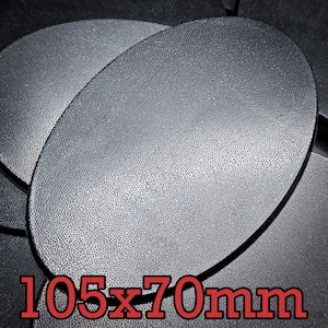 May include: A close-up of a black, oval-shaped, textured base with the dimensions 105 x 70 mm.