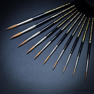 Puede incluir: Un conjunto de pinceles de pintura para artistas con mangos negros y virolas plateadas. Los pinceles están dispuestos en diagonal, mostrando sus puntas finas y puntiagudas. Cada pincel está etiquetado con números y la marca "Rosemary & Co Kolinsky Sable".