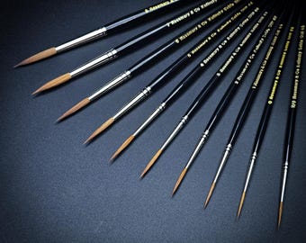 May include: A collection of artist paint brushes with black handles and silver ferrules. The brushes are arranged diagonally, showcasing their fine, pointed tips. Each brush is labeled with numbers and the "Rosemary & Co Kolinsky Sable" brand name.