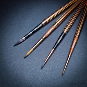 Könnte beinhalten: Vier Künstlerpinsel mit goldfarbenen Metallgriffen und dunklen Borsten. Die Griffe haben eine braune, holzähnliche Textur und der Markenname "Raphael" ist auf den Griffen aufgedruckt. Die Pinsel sind diagonal auf einer dunklen Oberfläche angeordnet.